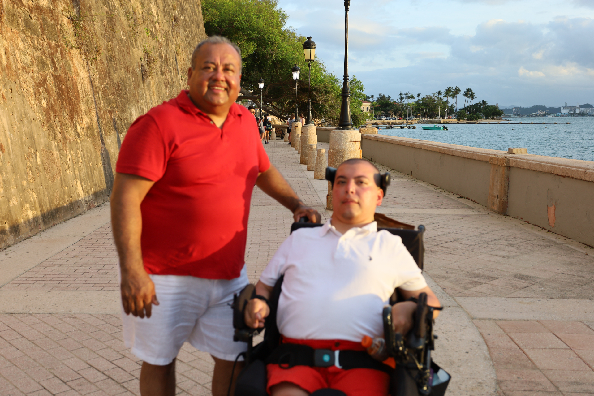 Raul as an adult in his wheelchair beside his dad Raul on a seaside walk in San Juan